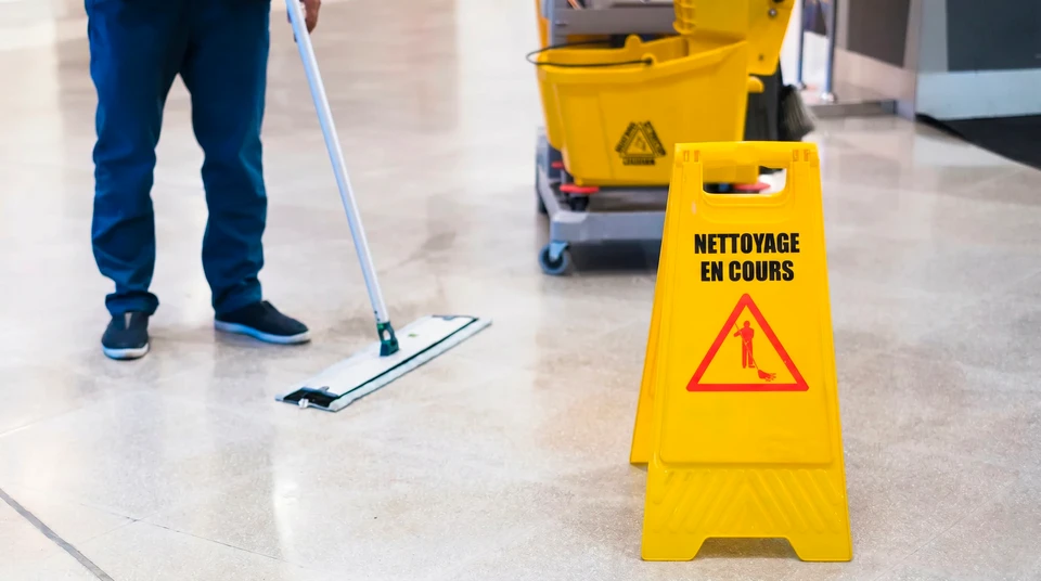 Scène intérieure de nettoyage professionnel avec agent d'entretien en uniforme blanc maniant un chariot de ménage
